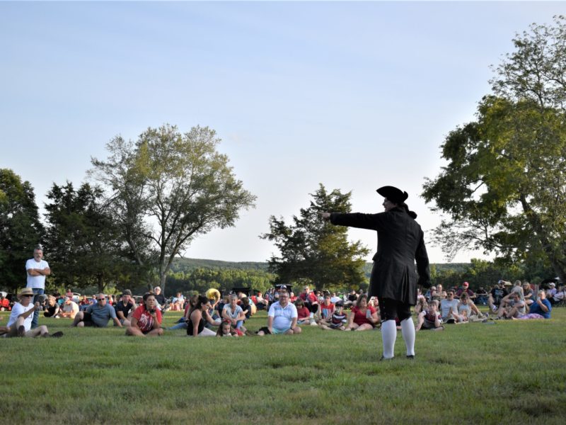 Man performing historical reenactment in front of a crowd sitting outside
